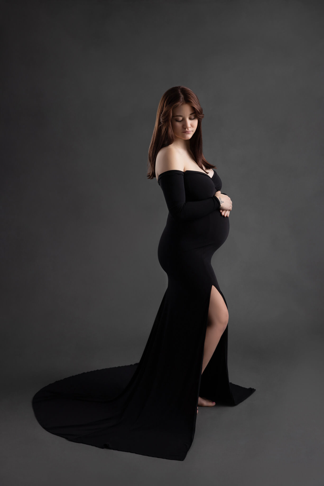 pregnant woman in an off the shoulder black fitted dress standing holding her bump looking at the ground