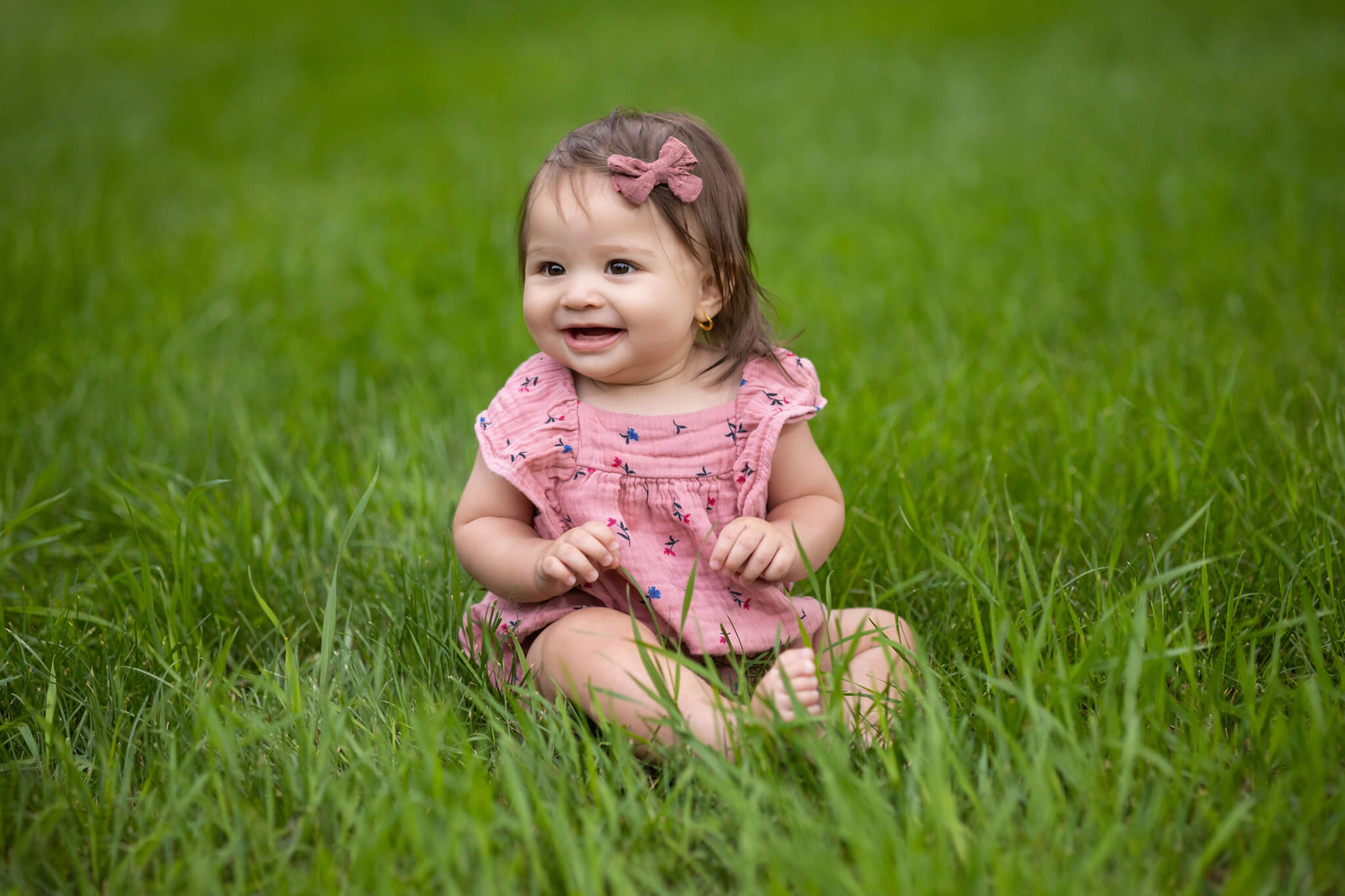 6 months old dark haired little girl sitting in a green grassy field in Beulah, CO
