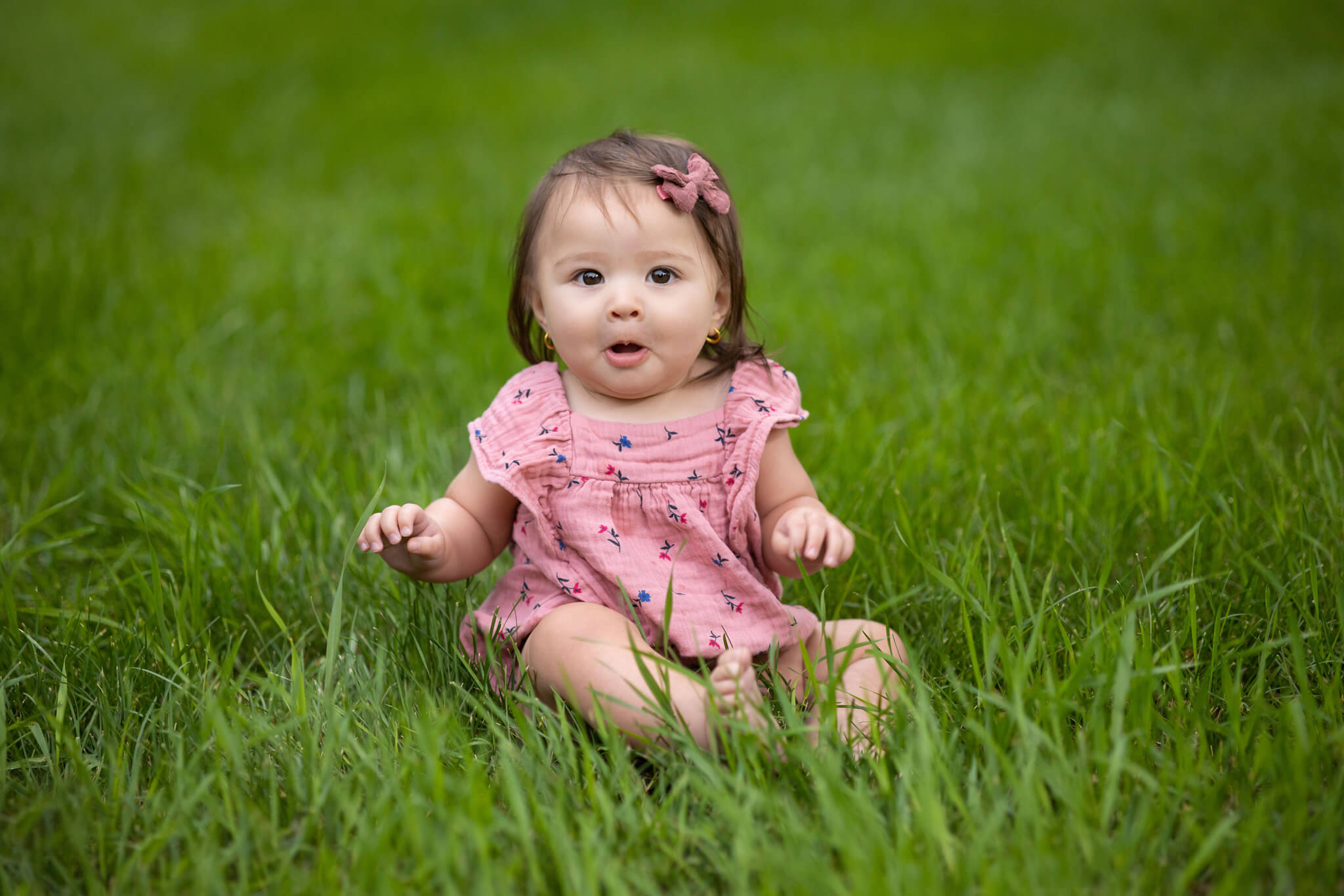 6 months old dark haired little girl sitting in a green grassy field in Beulah, CO