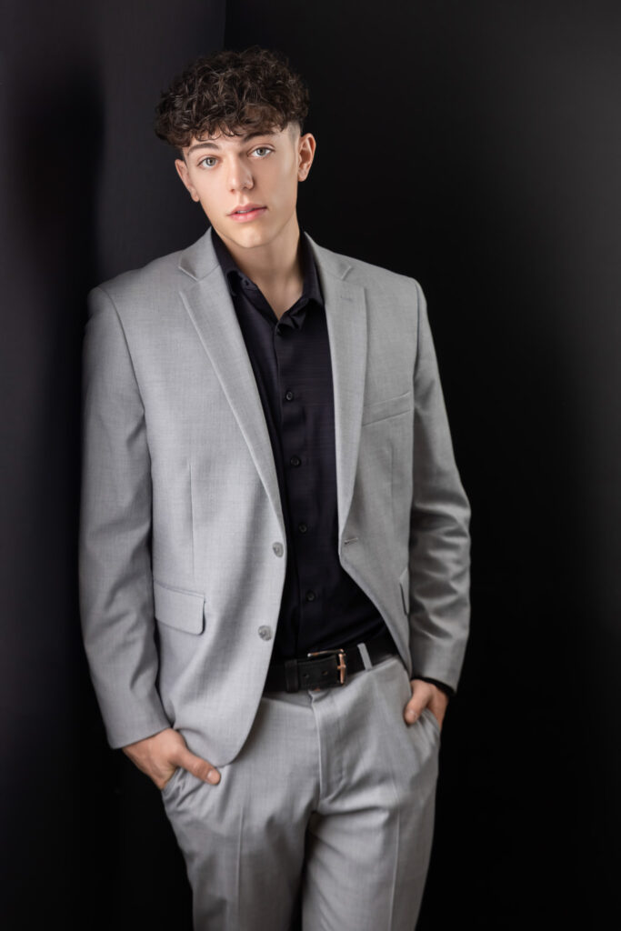 high school senior boy in a suit leaning against a wall