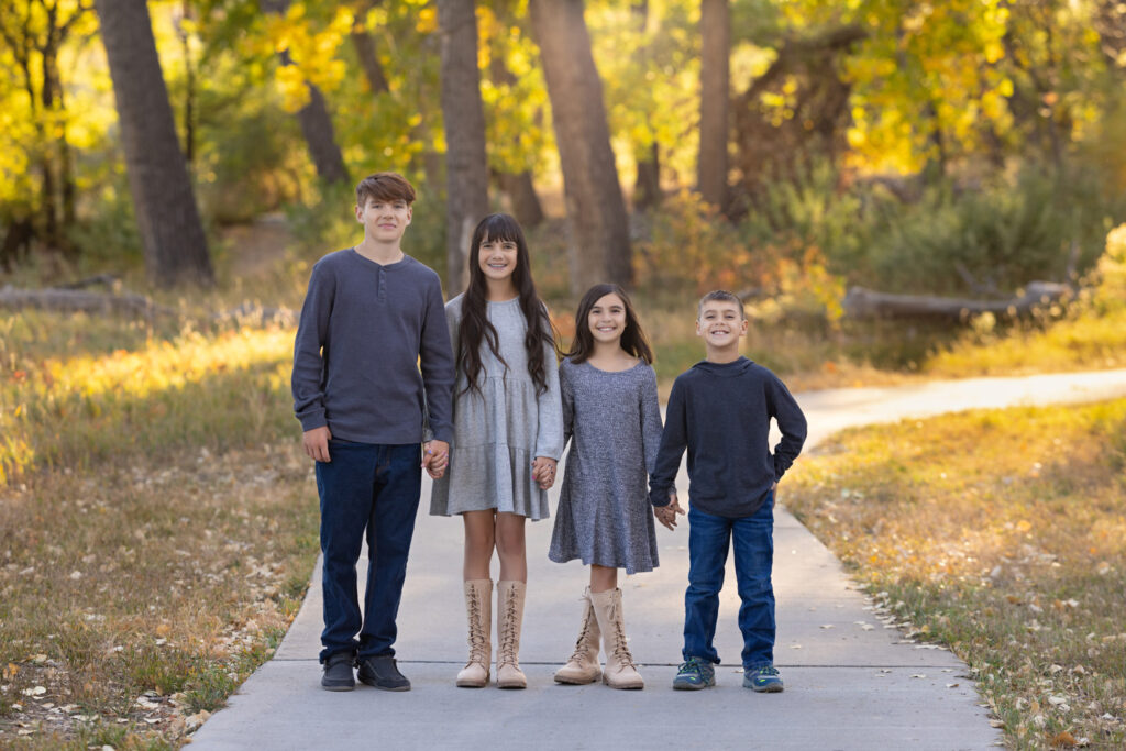 four siblings, two brothers and two sisters, standing shoulder to shoulder next to each other on a path at City Park in Pueblo