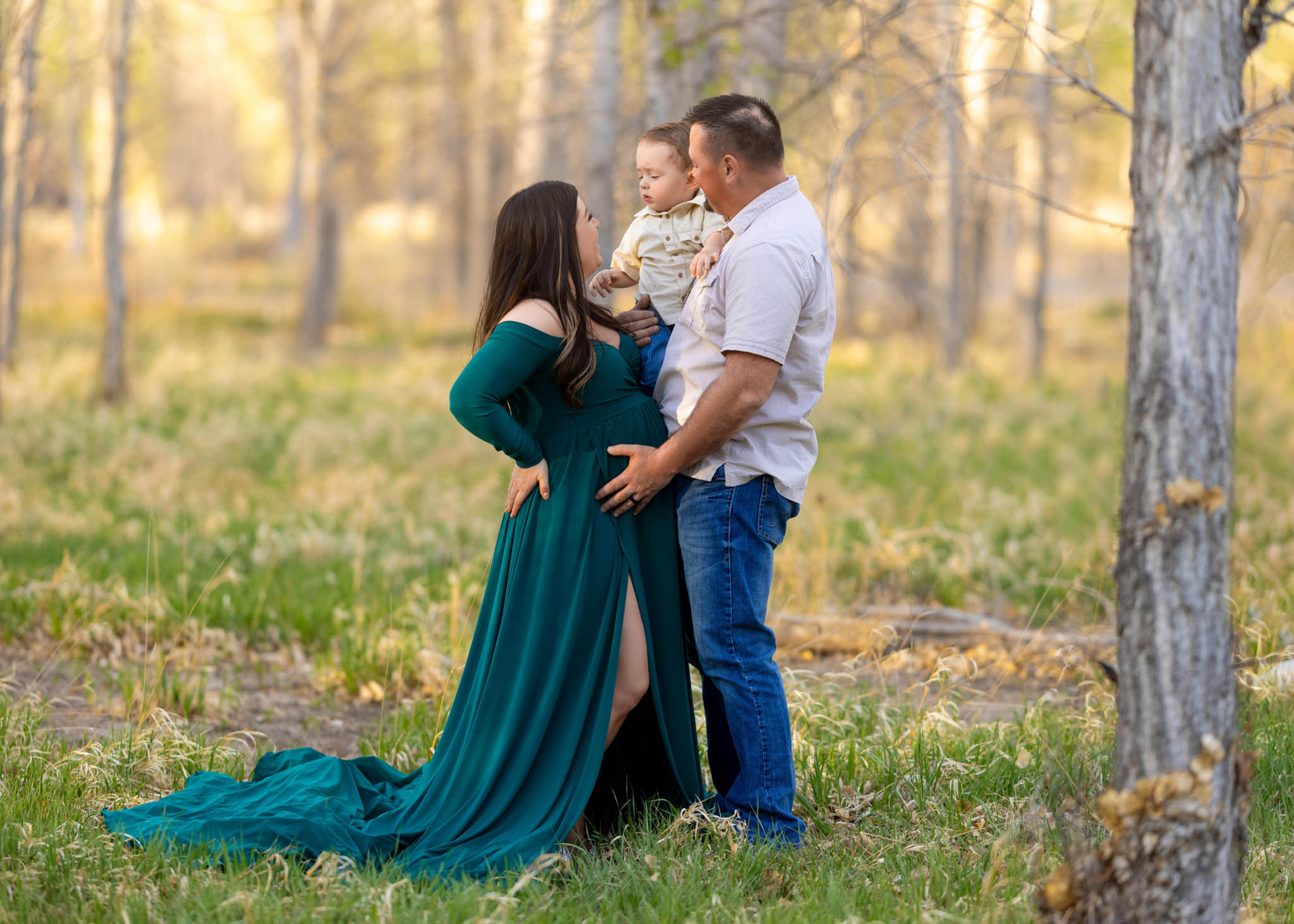 a pregnant mom with her 2 year old son and husband standing with each other in a field in City Park in Pueblo CO