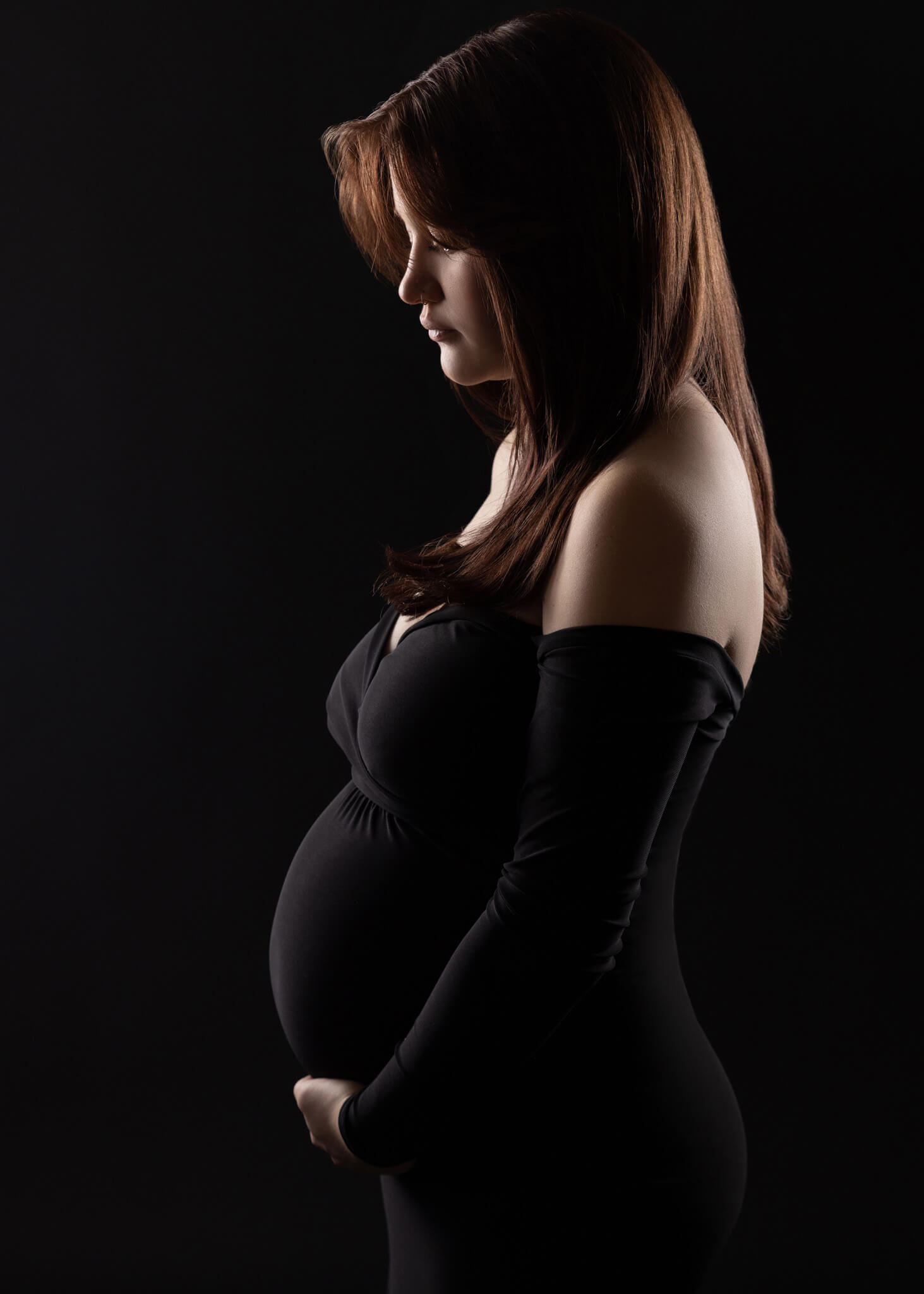 silhouette of a pregnant mom with long brown hair in a fitted black dress cradling her belly