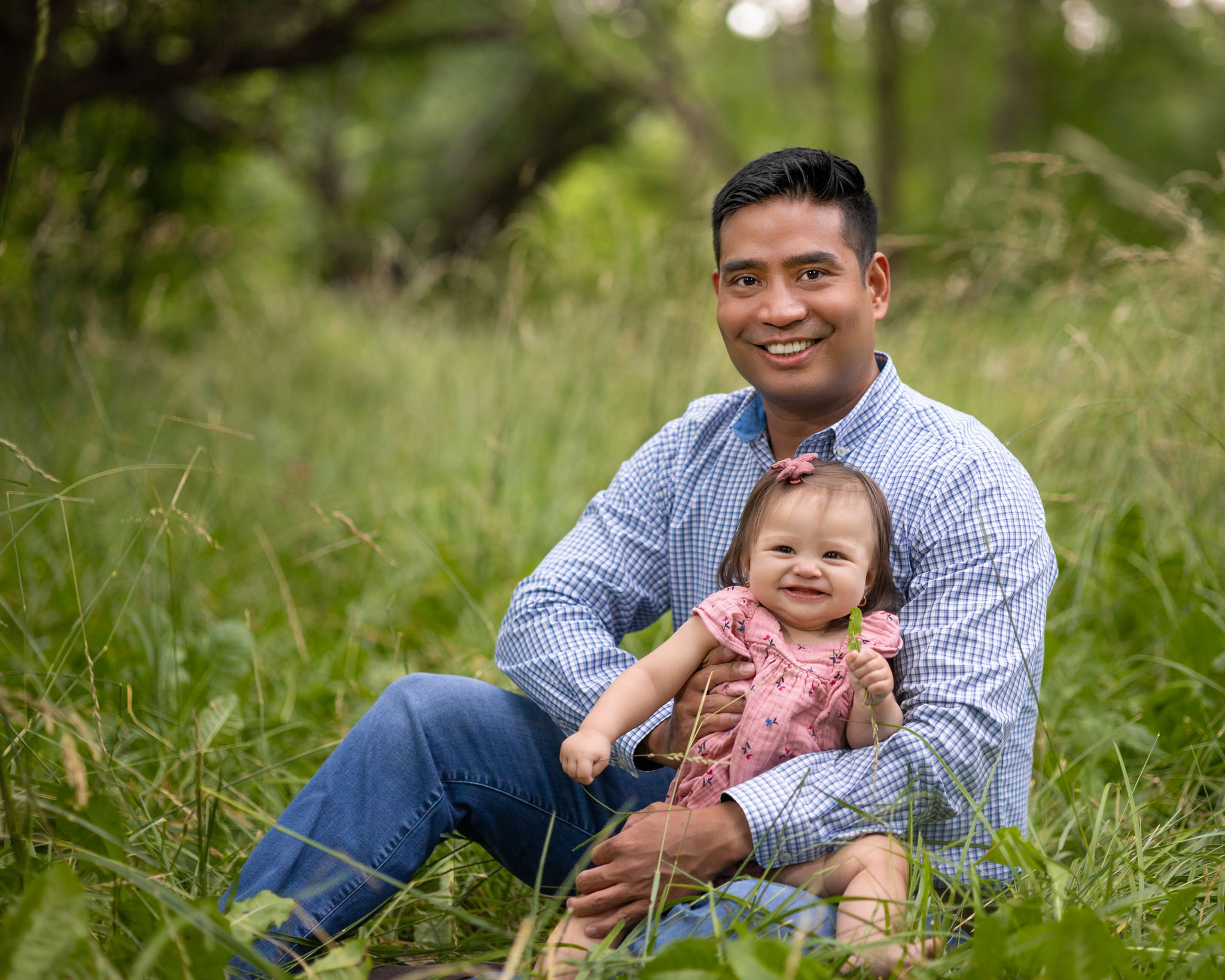dad and baby daughter sitting in a green grass field under trees in Pueblo CO