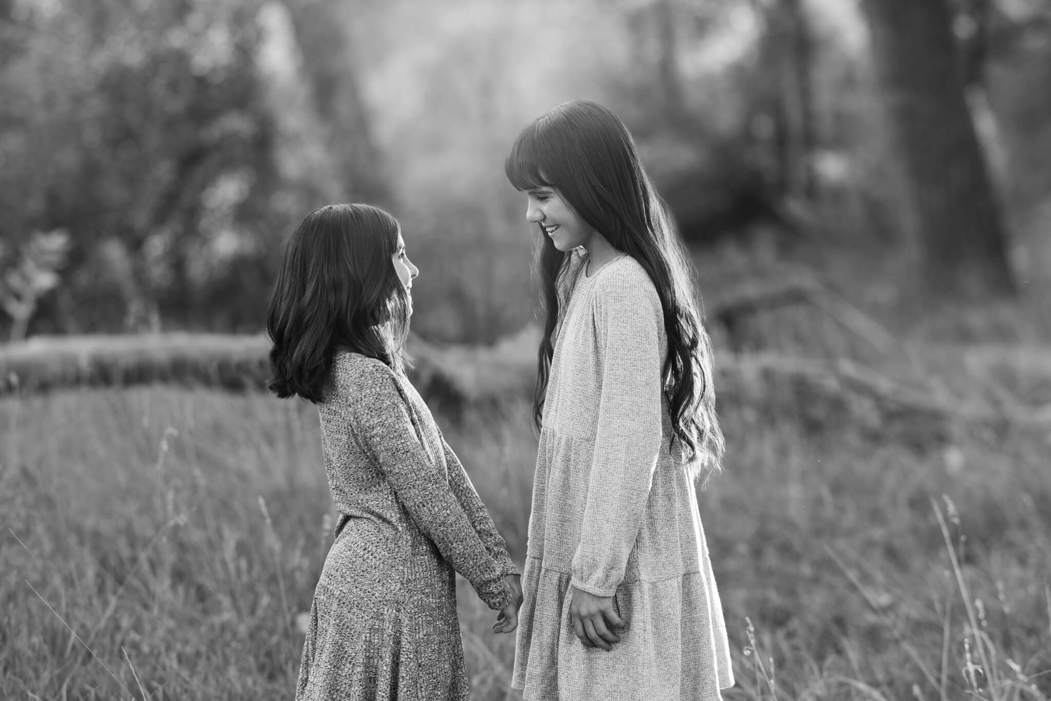 black and white image of two young sisters holding hands and look ing at each other in City Park in Pueblo CO
