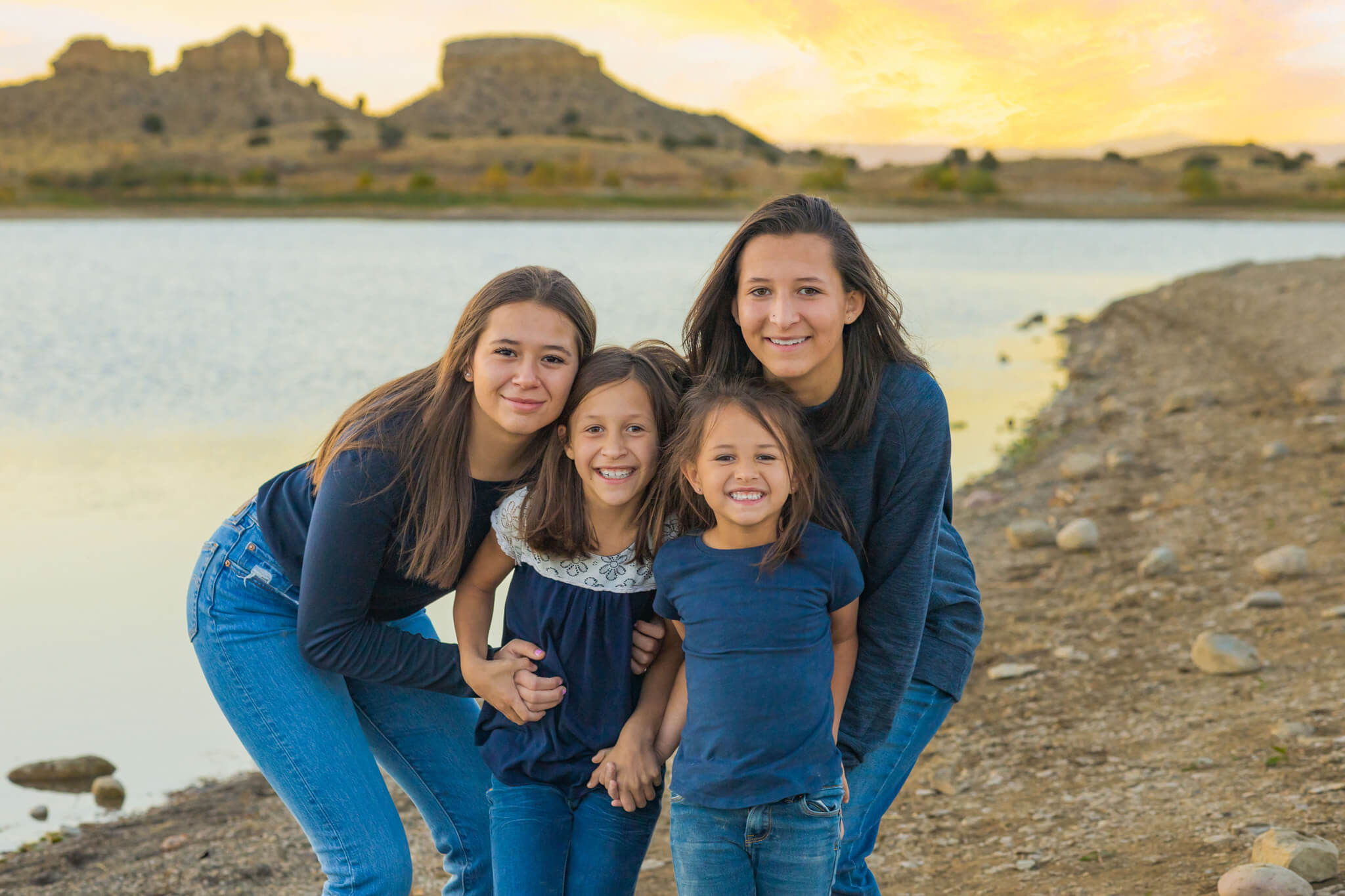 4 sisters standing snuggling close together on the beach at the Pueblo Reservoir at sunset