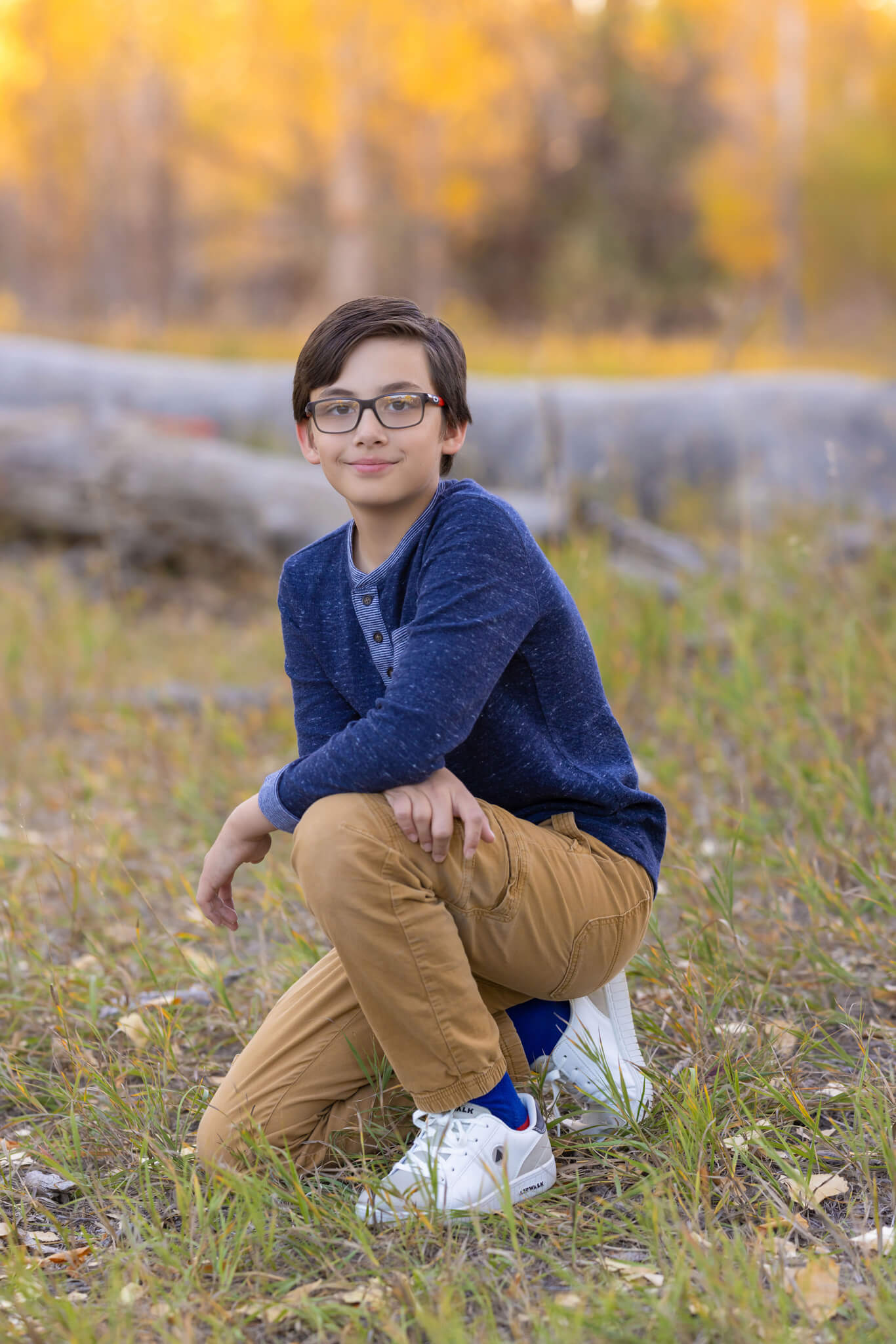 young boy with glasses crouching in fall colored grasses at City Park in Pueblo CO