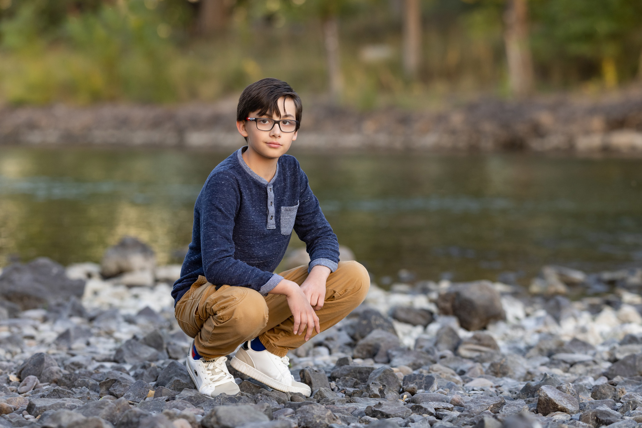 young brown haired boy with glasses crouching on the rocks next to the river at City Park in Pueblo CO